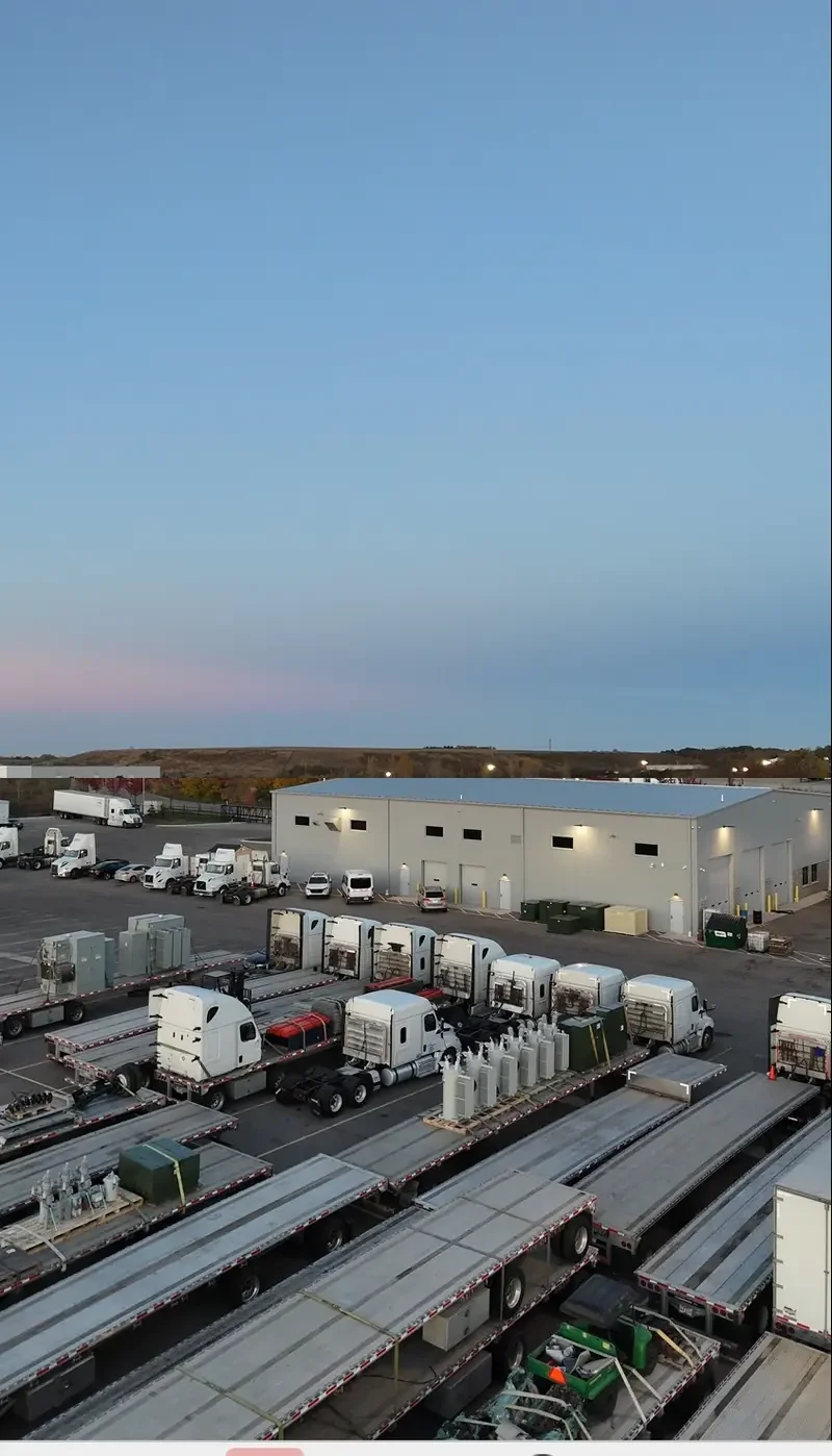 On-site repair shop building at dusk with lit windows and garage bay doors, viewed from the parking yard